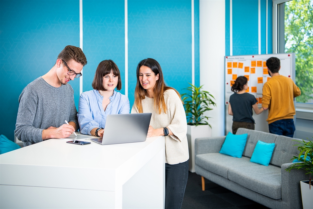 Drei DBM-Studierende im Vordergrund vor Laptop, zwei Studierende im Hintergrund am Flipchart-Board