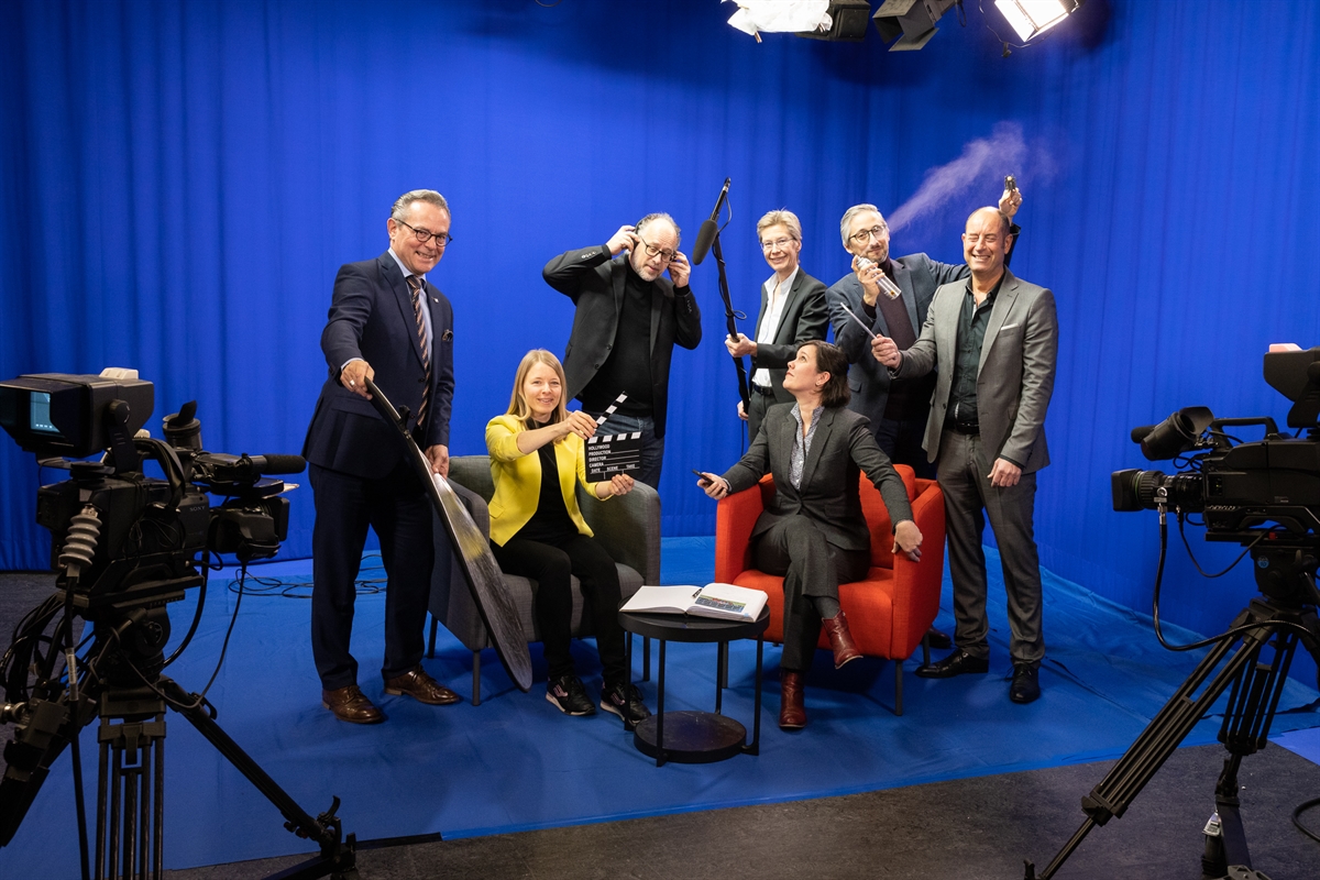 Sieben Personensetzen sich in einem Aufnahmestudio in Szene