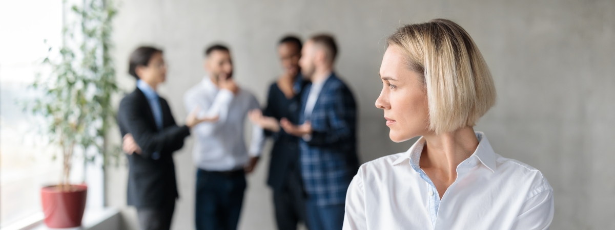 Eine Personengruppe im Hintergrund tuschelt offenbar über ein Person im Vordergrund