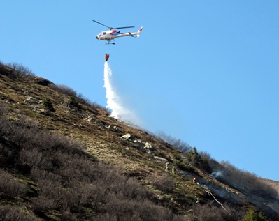 Löscharbeiten durch die Feuerwehr mit der Motorpumpe und einer Air Grischa-Helikopter Crew mit dem Wassersack