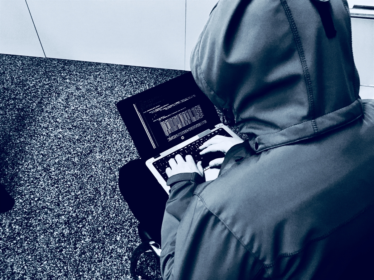 Von hinten gesehen: Eine unbekannte Person mit Kapuzenjacke vor seinem Bildschirm.