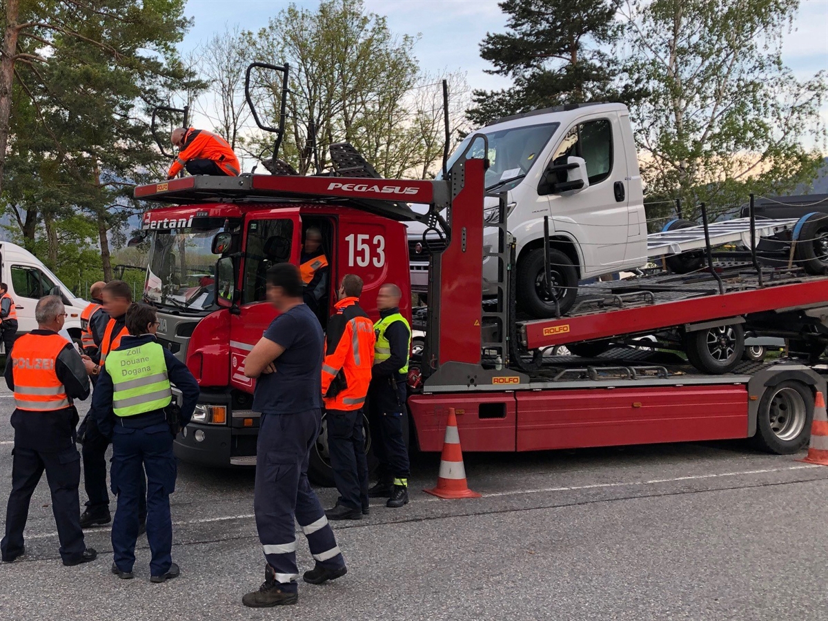 Ein auf dem Rastplatz stehender Autotransporter. Auf dessen Kabine ein kniender Polizist, welcher etwas misst. Weiter Einsatzkräfte, die um das Fahrzeug stehen.