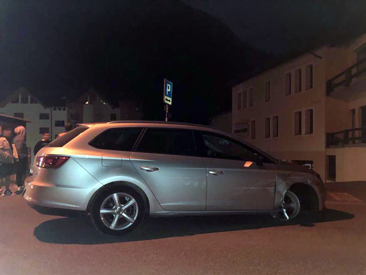 Das vorne rechts an der Radaufhängung total und an der rechten Fahrzeugseite stark beschädigte Auto. Dahinter Jugendliche und ein Polizist.