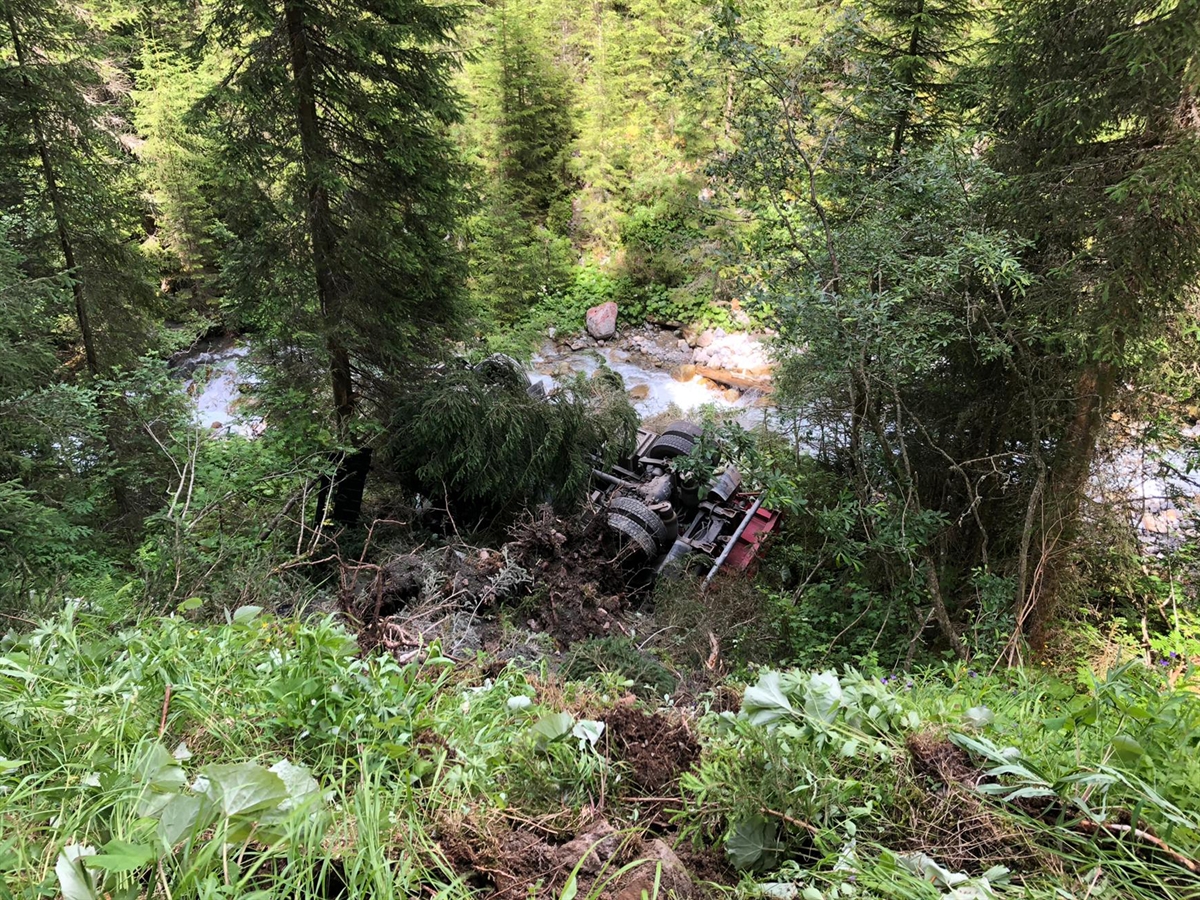 Der auf dem Dach neben dem Inneralpbach liegende Lastwagen zwischen Bäumen am Fusse der Böschung