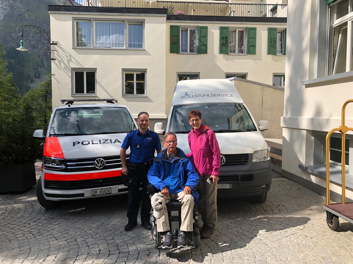 Der Rollstuhlfahrer mit der Polizeipatrouille und seiner Frau vor dem Polizeiauto und dem Rollstuhltransporter.