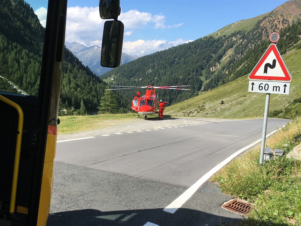 Die Umbrailstrasse, links auf einem Ausstellplatz der Rega-Helikopter. Rechts am Strassenrand ein Gefahrensignal 