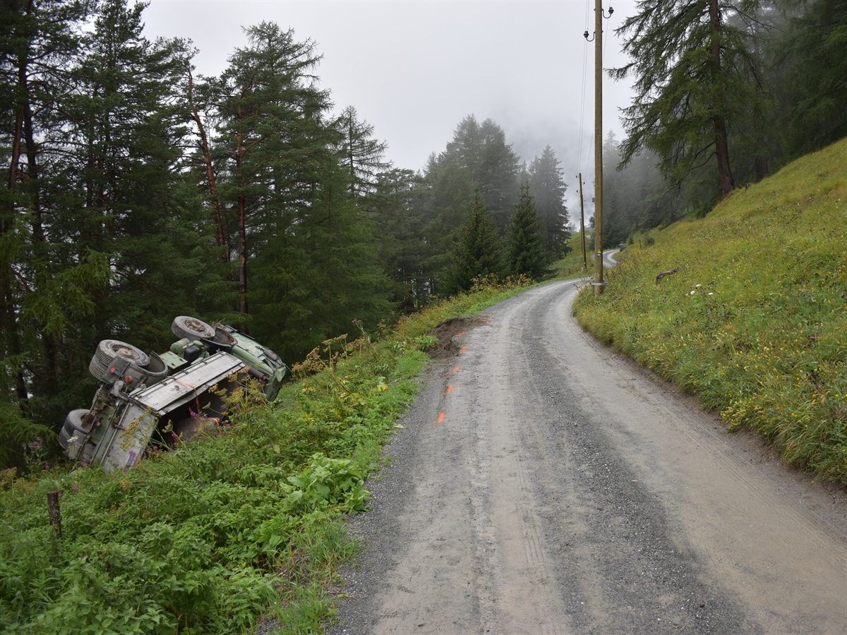 Abgestürzter Lastwagen neben der Strasse auf der Seite liegend.
