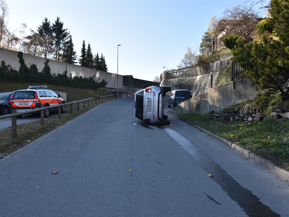 Das Auto liegt seitlich liegend auf der Strasse. Rechtsseitig die ansteigende Stützmauer.