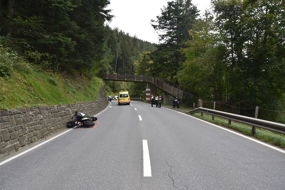 Übersichtliche Kurve. Auf der linken Seite Stützmauer und auf Fahrbahn beschädigtes Motorrad.
