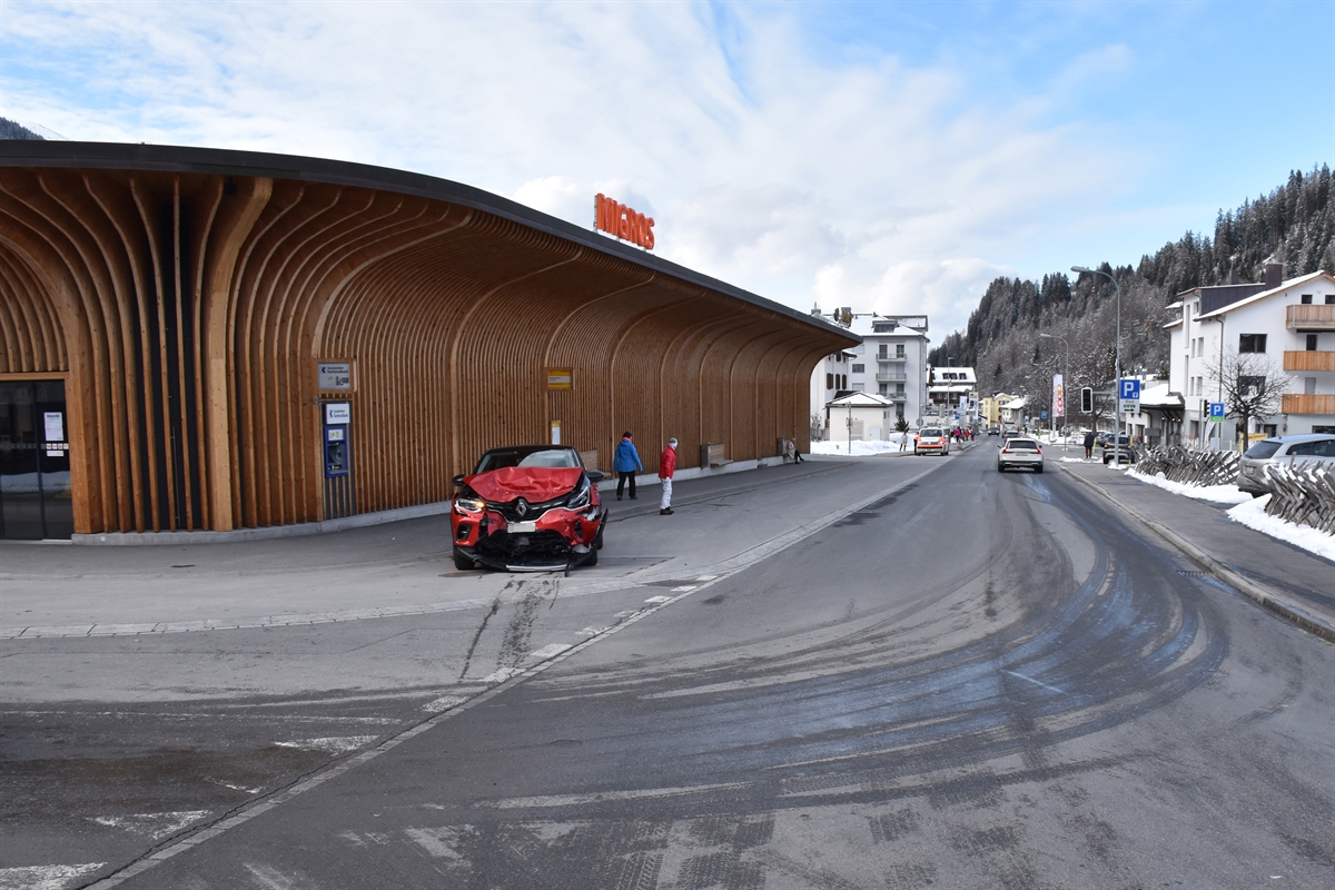 Die Strasse, links das frontal total beschädigte Auto der Frau. Im Hintergrund ein Verkaufsgeschäft. Rechts im Bild die Strasse talwärts gesehen.