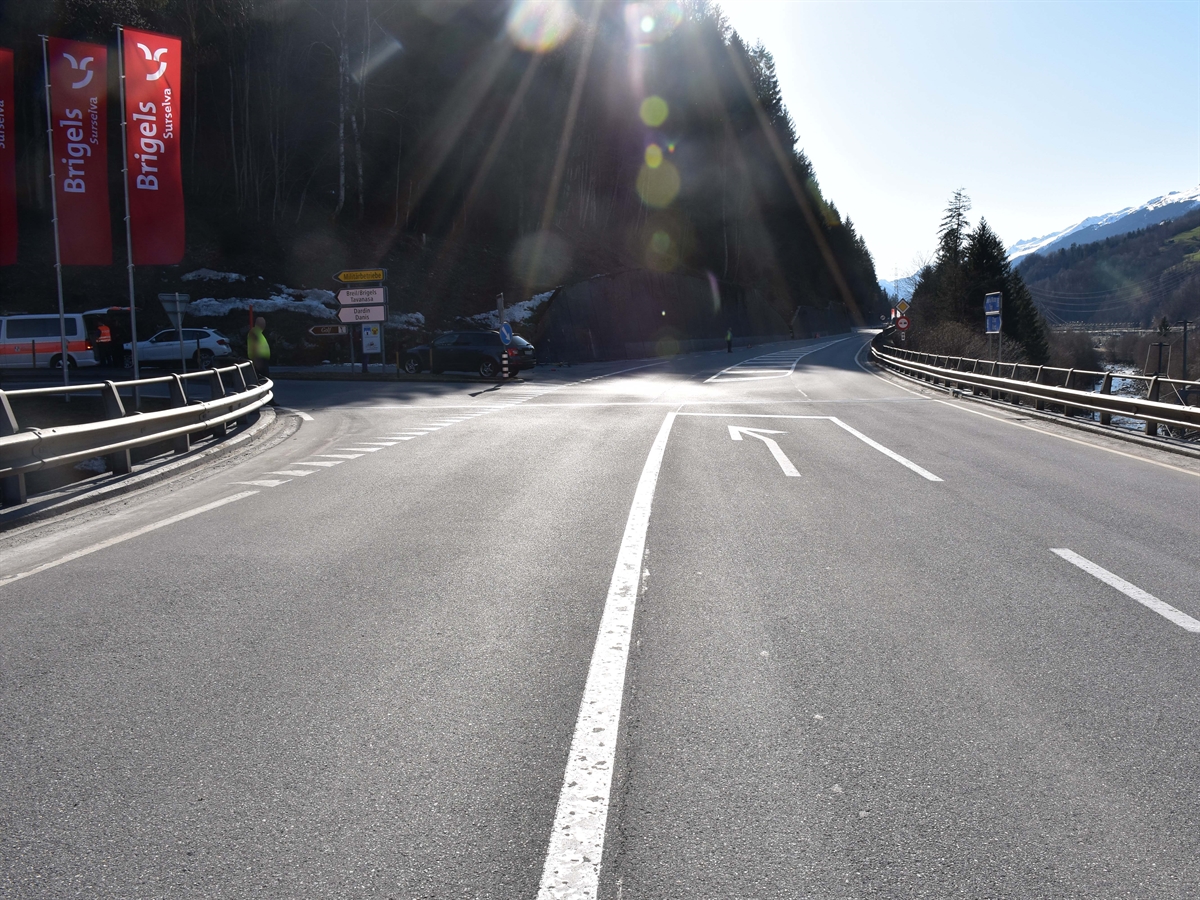 Die Oberalpstrasse mit Linksabbiegespur nach Tavanasa / Danis. Private Personen regeln den Fahrzeugverkehr. Auf der Zufahrt nach Danis stehen ein Patrouillenfahrzeug sowie zwei Personenwagen. Das Rennfahrrad liegt links am Rand der Oberalpstrasse.