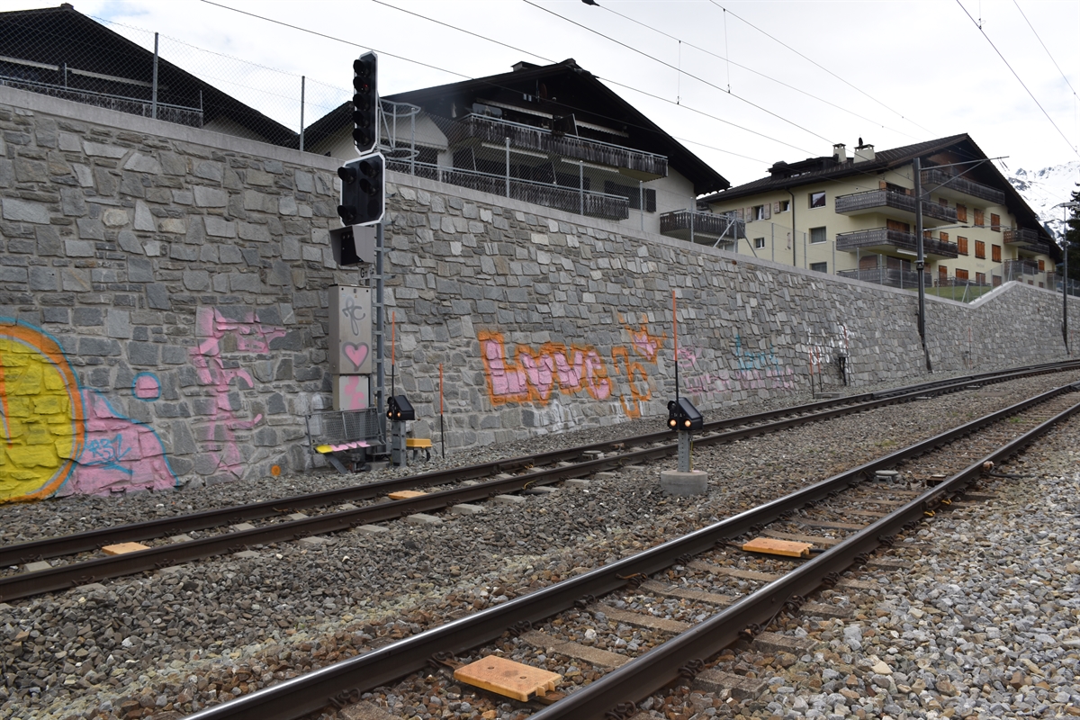 Im Vordergrund Geleise, dahinter eine versprayte Stützmauer sowie versprayte Signalanlage.