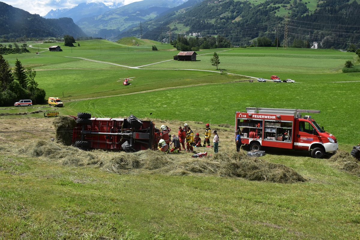 Wiesland, links im Bild der Ladewagen mit Blick auf den Unterboden. Rechts davon Rettungskräfte und ein Feuerwehrfahrzeug. Links davon im Hintergrund eine Ambulanz, ein Polizeifahrzeug und etwas weiter weg der Rega-Helikopter.