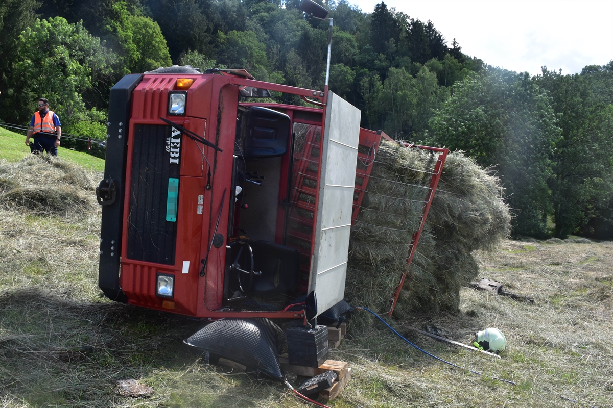 Der auf der Fahrerseite liegende Ladewagen von vorne. Die gekippte Ladefläche ist mit Heu gefüllt. Links neben dem Fahrzeug im Hintergrund ein Polizist.