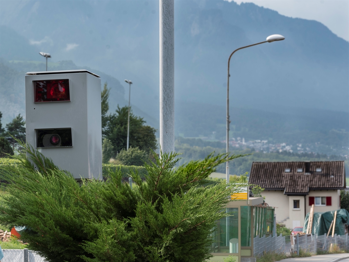 Links eine semistationäre Geschwindigkeitsmessanlage. Rechts davon Umgebung und der Randbereich einer Strasse.