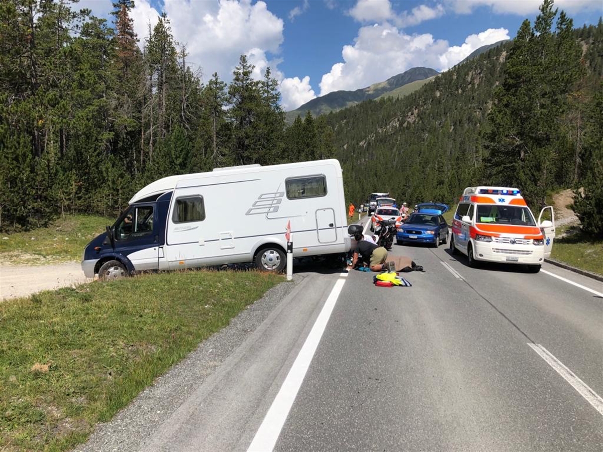 Links ein quer direkt an der Strasse stehendes Wohnmobil. In dessen Heckbereich Rettungskräfte und eine mit einer Decke zugedeckte Person. Rechts davon (auf der Strasse) ein Ambulanzfahrzeug.