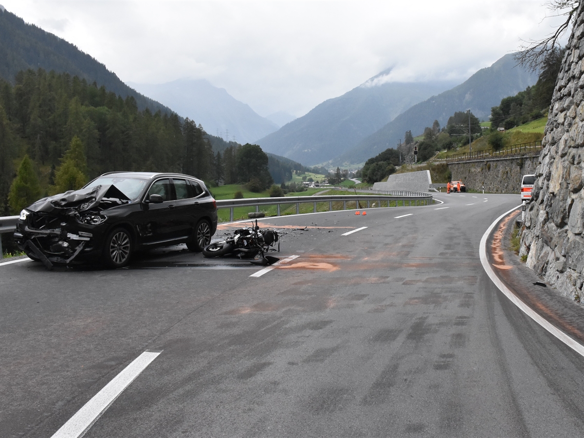 Blick von vorne auf die Strasse. Ein an der Front stark beschädigtes Auto und rechts daneben auf der Seite liegend ein total beschädigtes Motorrad. Im Hintergrund ein Polizeiauto.