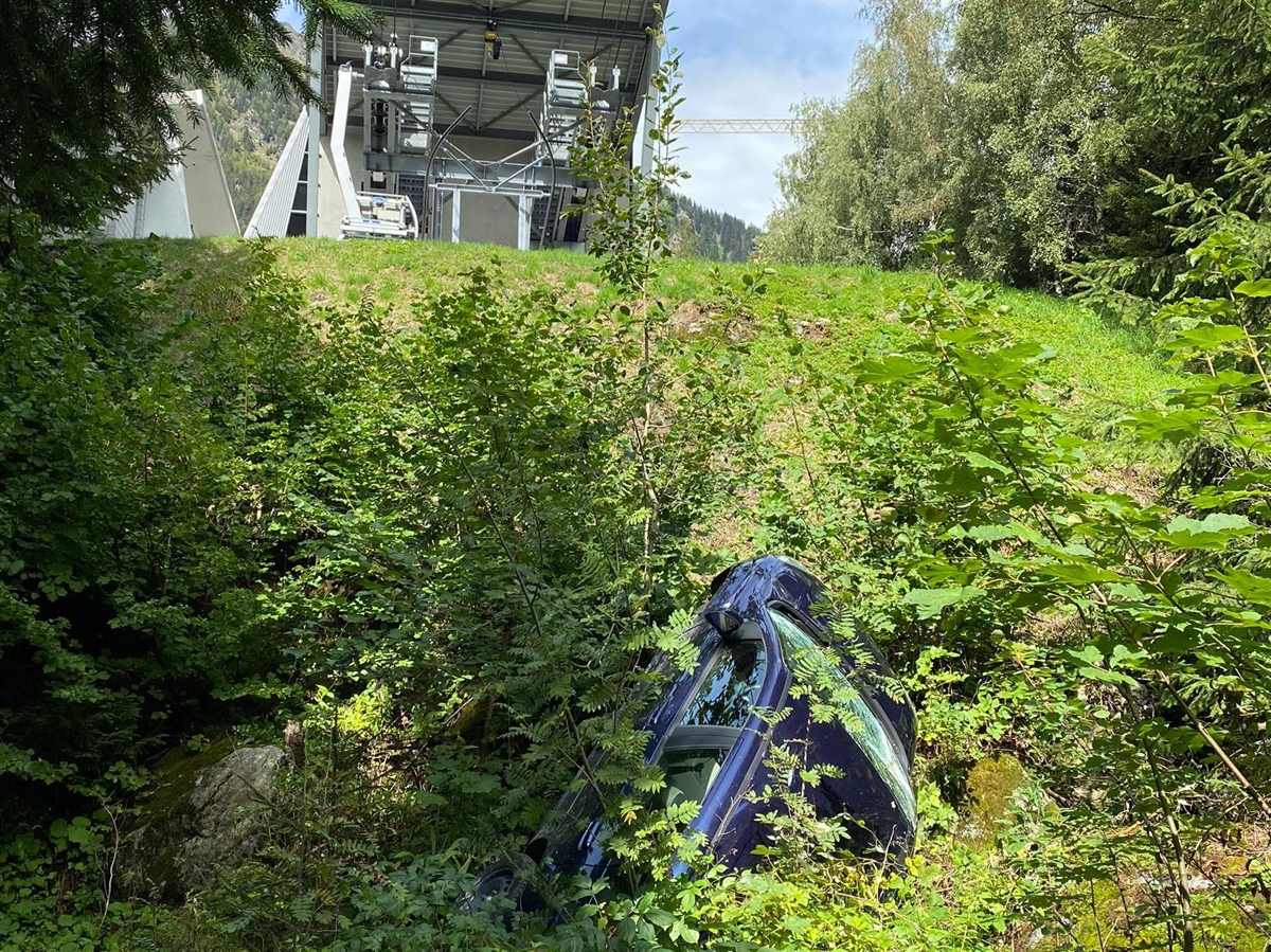 Frontale Sicht auf den abfallenden Hang. Inmitten von Gebüsch ein total beschädigtes Auto.