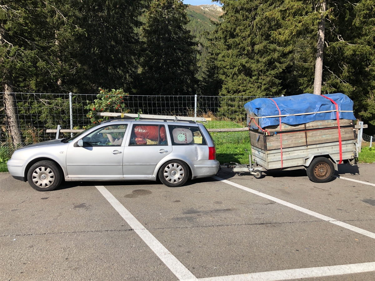 Seitliche Aufnahme der Fahrzeug-kombination. Durch die Scheiben des Autos ist dessen Beladung sichtbar. Die Vorderachse ist offensichtlich ent- und die Hinterachse belastet. Offensichtlich auch, wie der Anhänger stark auf der Anhängerkupplung des Autos lastet.