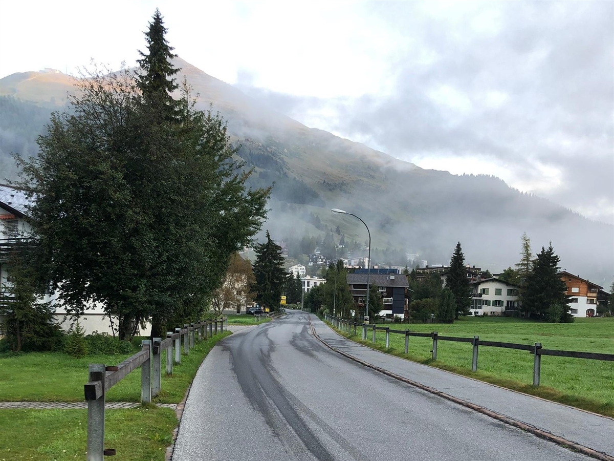 Die Dischmastrasse, rechts ein Trottoir. Im Hintergrund Häuser.