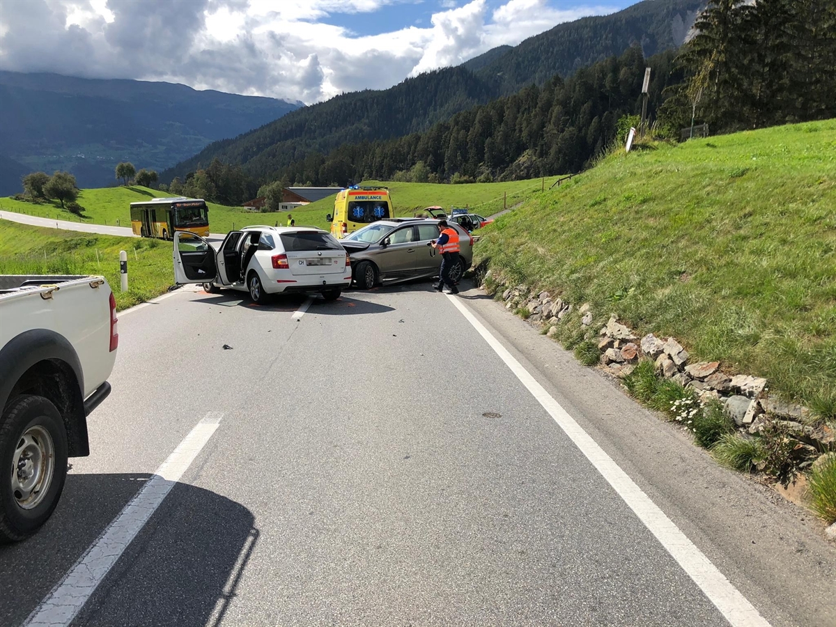 Die beiden Unfallfahrzeuge auf der Landwasserstrasse. Im Hintergrund die Ambulanz der Rettung Mittelbünden sowie ein wartendes Postauto. Ein Polizist erstellt Schadenfotos der Unfallfahrzeuge.