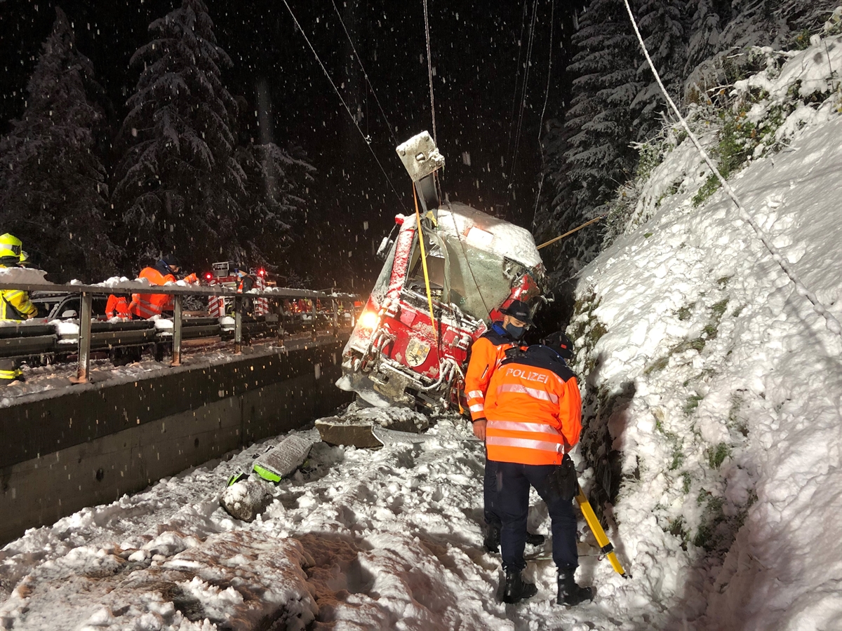 Steuerwagen der RhB steht schräg auf den Gleisen. Im Vordergrund stehen zwei Polizisten und auf der linken Bildseite sind weitere Einsatzkräfte der Bahnrettung Feuerwehr Thusis ersichtlich.