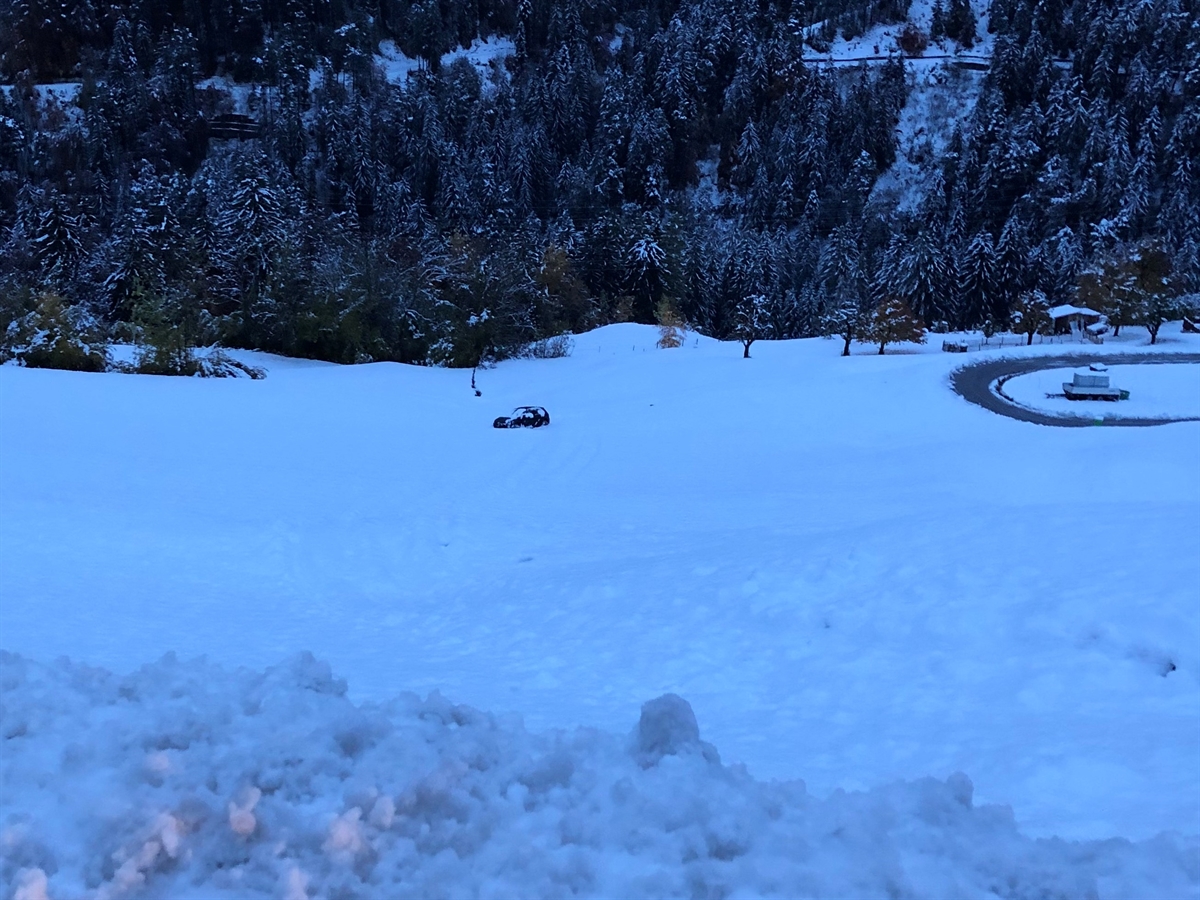 Aufnahme in das abfallende verschneite Wiesland. Inmitten diesem steht das Auto.
