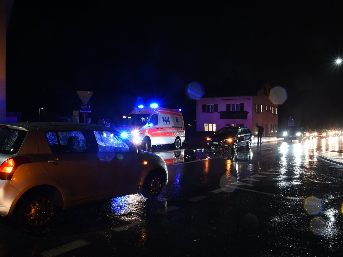 Aufnahme in abgeschlossener Abenddämmerung. Links im Vordergrund der Kleinwagen, quer über die von links nach rechts: Die Ambulanz mit Blaulicht, das Velo am Boden, direkt daran das auf der Gegenfahrspur genahte Auto. 