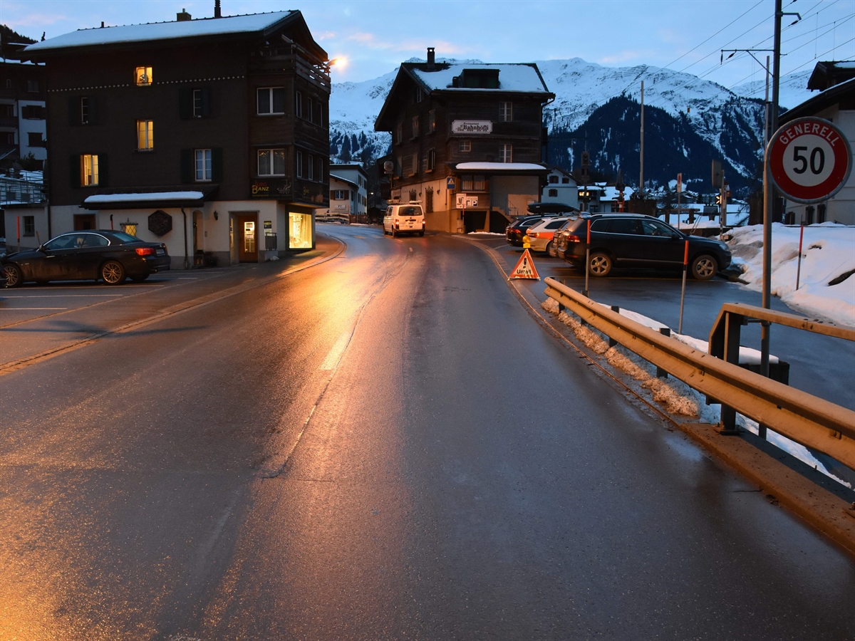 Die Strasse, welche im hinteren Bildteil eine Linkskurve macht. In dieser Linkskurve ein Lieferwagen auf der rechten Spur auf dem Fussgängerstreifen. 