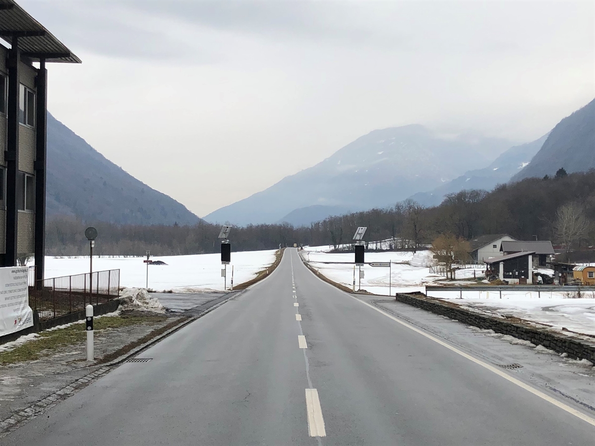 Übersichtsaufnahme der H13 in Richtung San Vittore. Eine längere Gerade, im Vordergrund links ein Gebäude. Links und rechts je eine Zufahrt in die H13.  