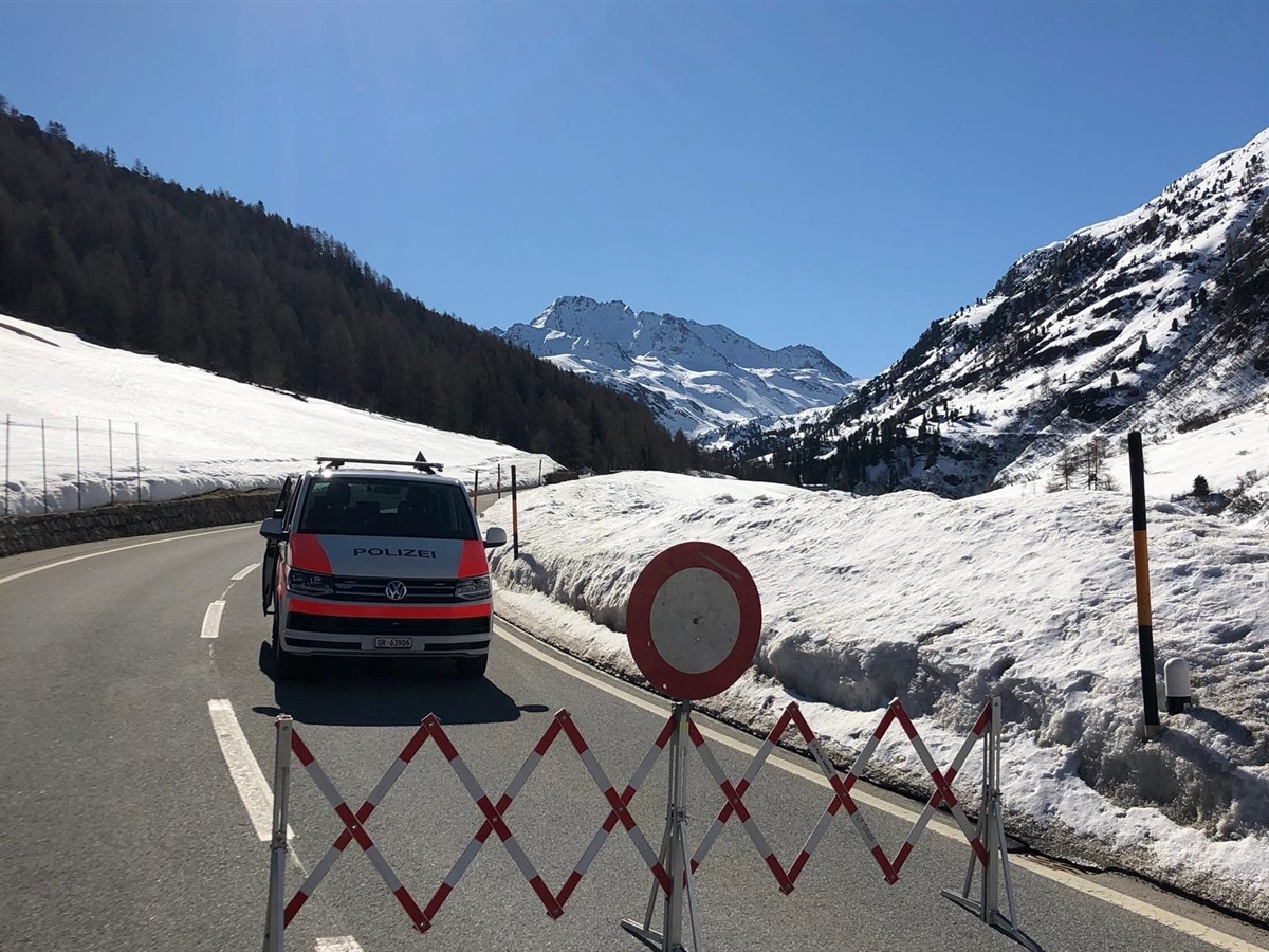 Patrouillenfahrzeug hinter einen Scherengitter mit einem allgemeinen Fahrverbot. Wunderbare Winterlandschaft inmitten der Bündner Berge mit stahlblauem Himmel