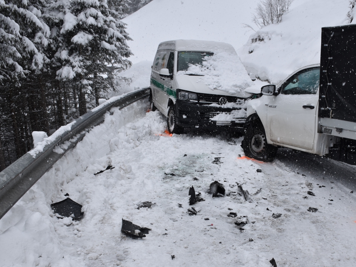 Eine verschneite Strasse. Rechts der talwärts gefahrene Lieferwagen mit zusammengestossener Front direkt an den bergwärts gefahrenen Lieferwagen. Kollisionsteile auf der Fahrbahn.