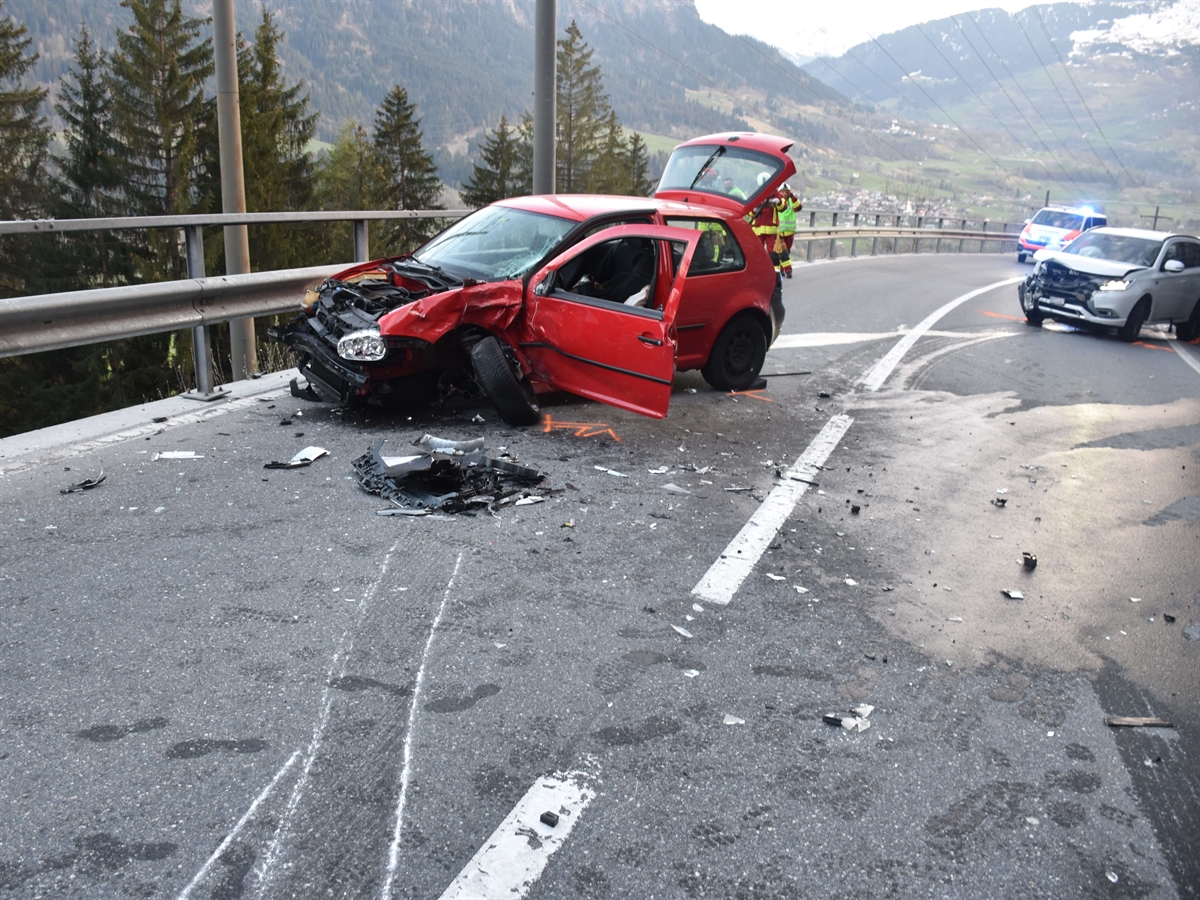 Auf der linken Fahrbahnhälfte ein rotes total beschädigtes Auto. Rechts, ein Stück weiter unten, das zweite, an der Front stark beschädigte Auto.  