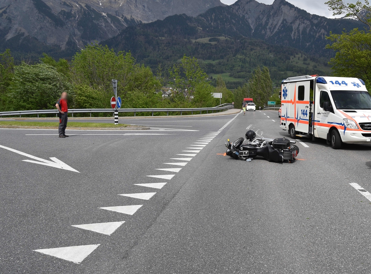 Rechts ein Ambulanzfahrzeug auf der Strasse, links davon das am Boden liegende Motorrad. Weiter links die Zufahrt zur A13. Im Hintergrund Berge.