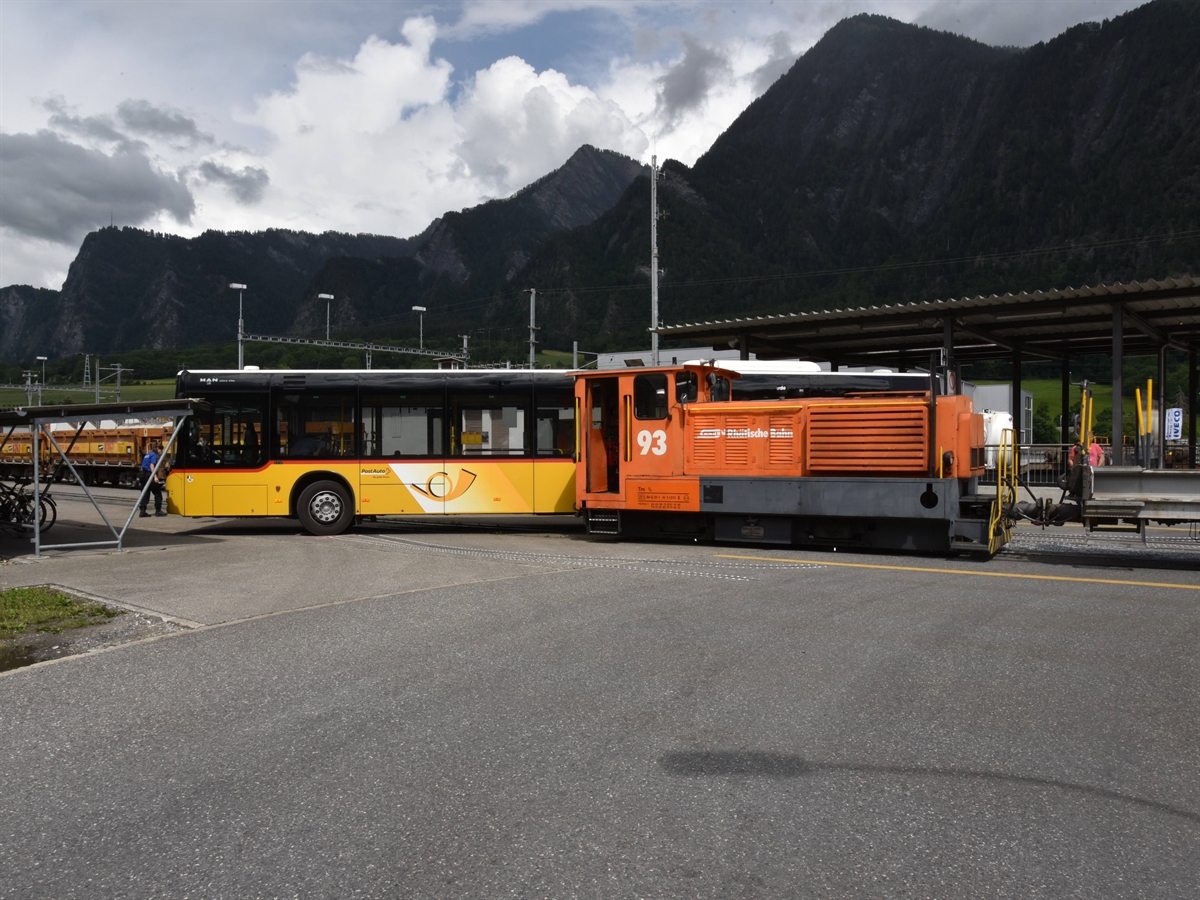 Links ein Postauto, rechts davon eine Rangierlokomotive. Im Vordergrund sind Reifendruckspuren erkennbar, als das Postauto von der Lokomotive geschoben wurde. Links vom Postauto ein Polizist. Im Hintergrund Bergpanorama.