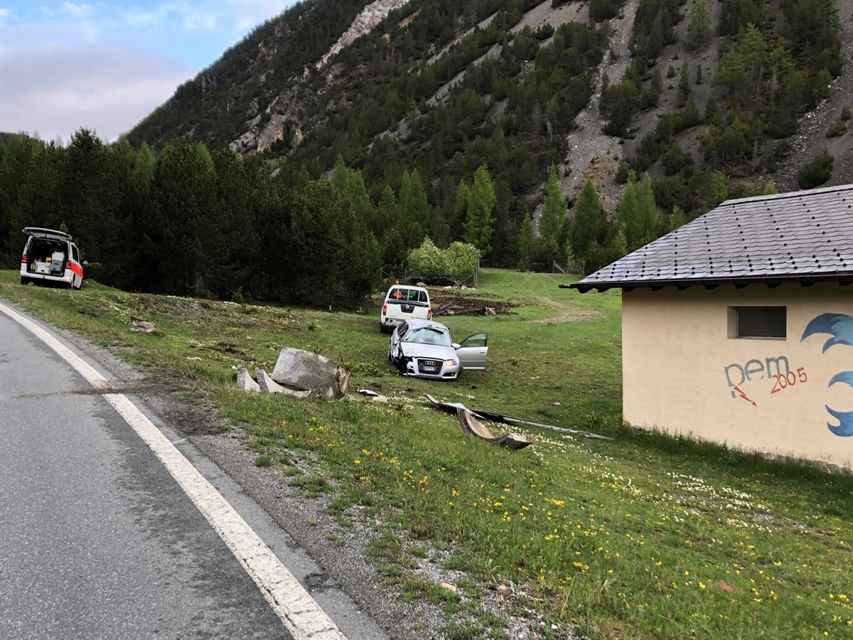 Fahrbahnrand der Ofenbergstrasse mit umgefahrenem Signalsockel. Hinter diesem das total beschädigte Auto auf der Wiese. In der Nähe stehen ein Patrouillenfahrzeug sowie ein Zivilfahrzeug des Strassendienstes
