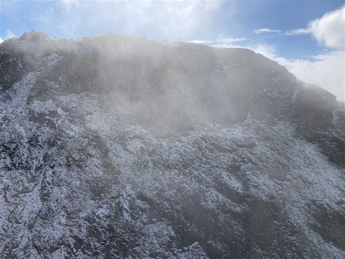 Die leicht angeschneite Südostflanke des Gipfels Uf da Flüe. Im Hintergrund blau-weisser Himmel.