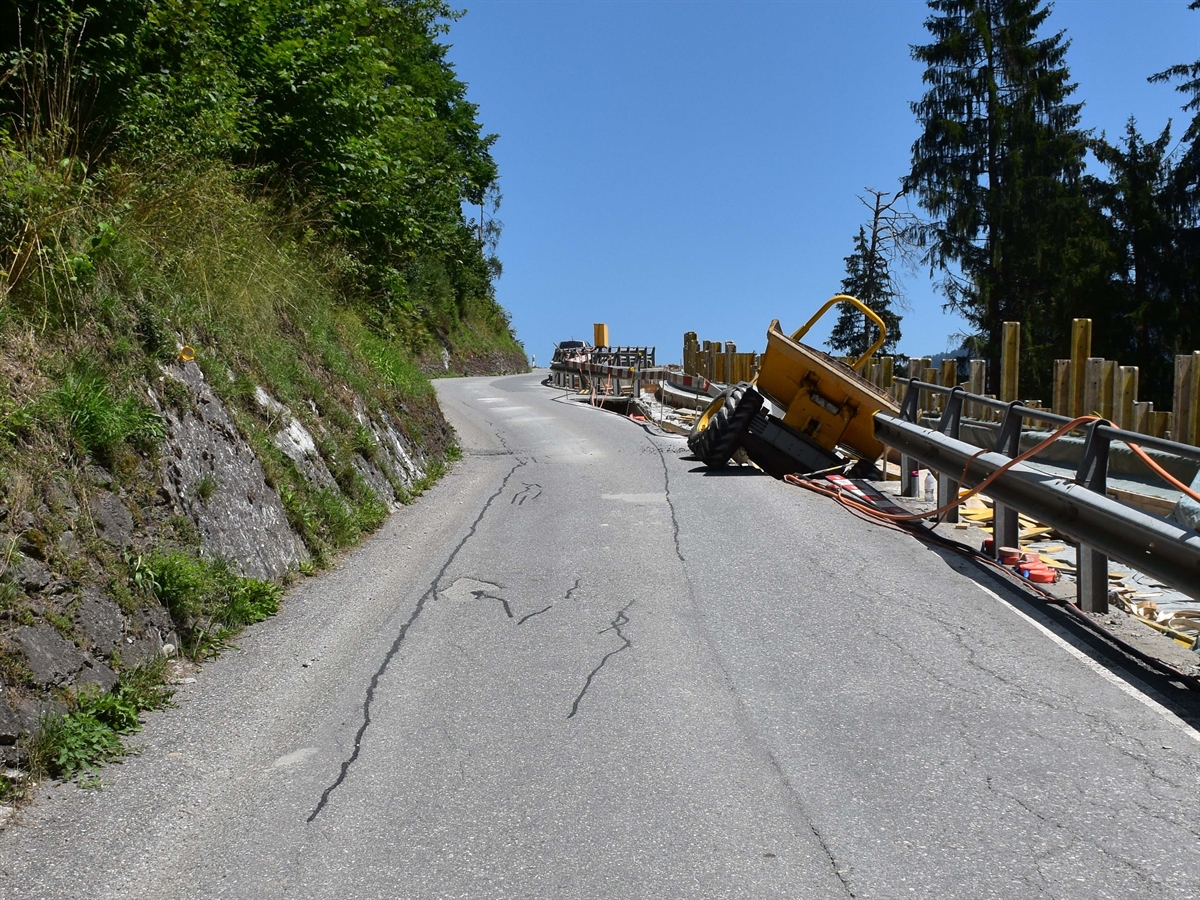 Links als Abgrenzung zur Strasse steile Hangmauern. Rechts die Ladirerstrasse, an deren Rand von vorne der seitlich teilweise in den Baustellengraben gekippte Motorkarren. 