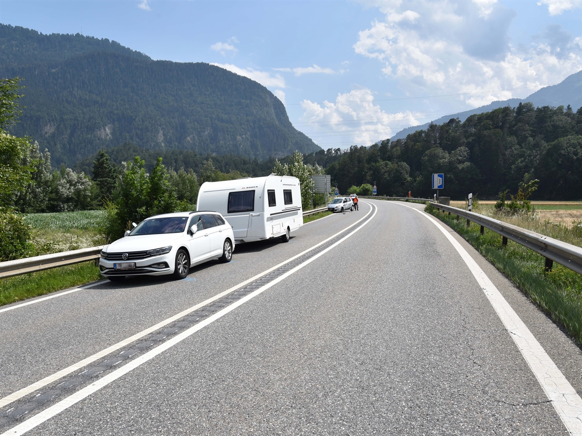 Die Unfallstelle auf der A13 aus Richtung Chur gesehen. Links das Wohnwagengespann von schräg vorne. Im Hintergrund auf derselben Strassenseite das beschädigte eingefahrene Auto und ein Polizist.