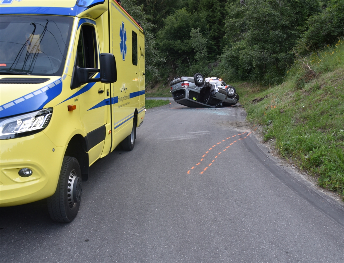 Rechtskurve von Cagliatscha Davains in Richtung Andeer. Im Vordergrund links ein Rettungswagen. Auf der rechten Seite das auf dem Dach liegende Auto. Dahinter ist noch ein Polizeifahrzeug zu erkennen.