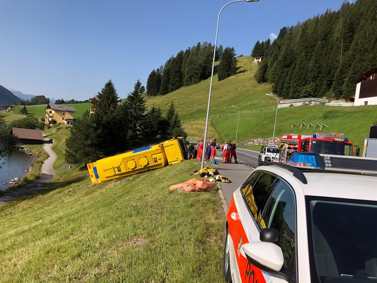 Im Hintergrund blauer Himmel. Links im Wiesland der Tanklastwagen. Rechts davon Feuerwehrleute, ein Polizeiauto und ein Feuerwehrauto.