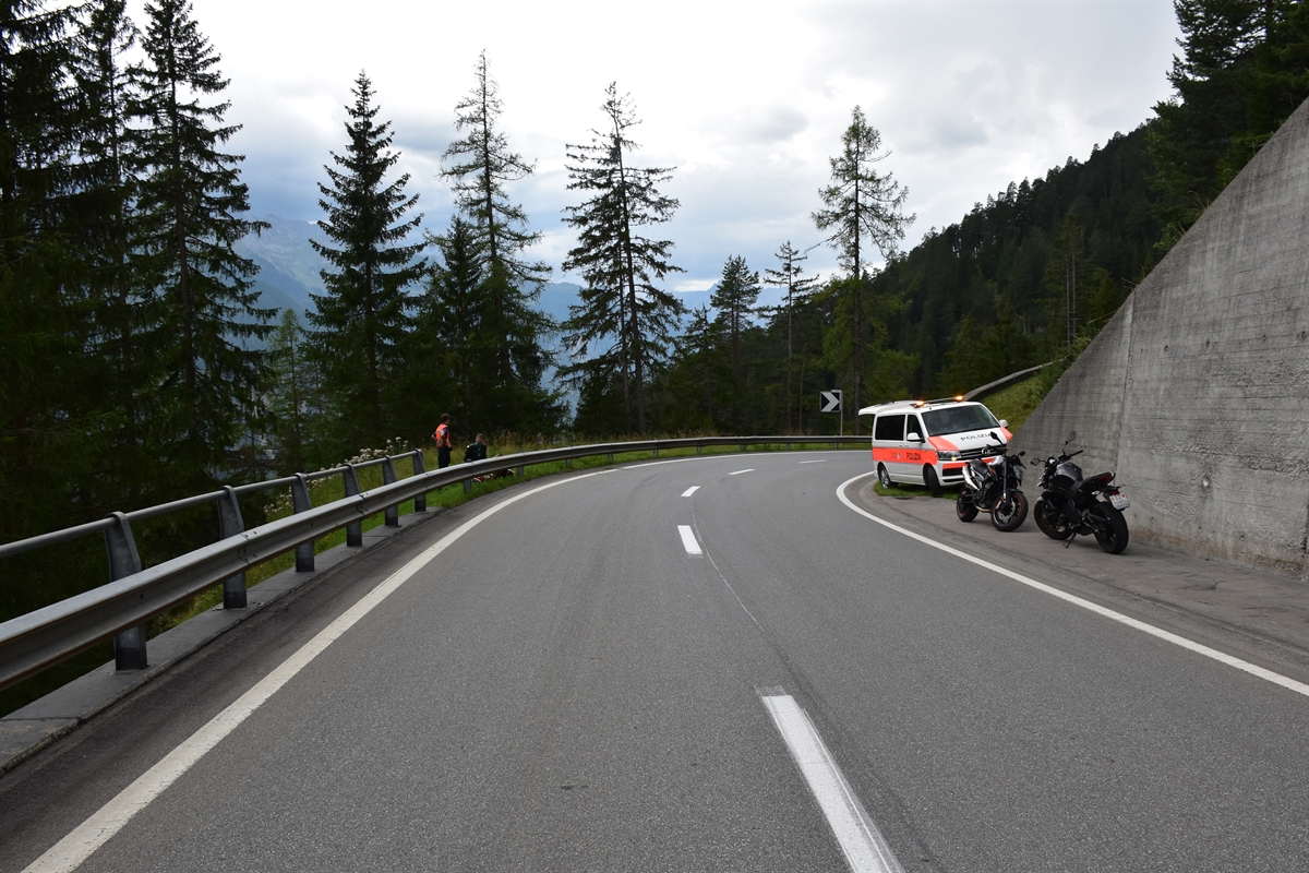 Strassenverlauf mit Rechtskurve. Rechts neben der Strasse stehen zwei Motorräder und das Polizeifahrzeug.