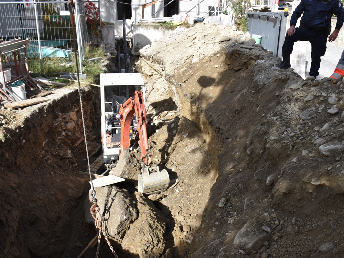 Der Bagger steht im Graben. Im vorderen Bereich ist die Maschine mit Erdmasse zugeschüttet. Auf dem Wall bei der Abbruchstelle steht ein Polizist.