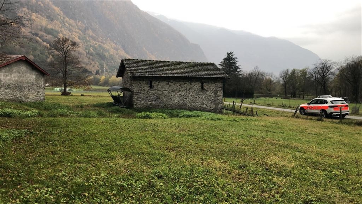 Unfallstelle in Grono. Im Vordergrund eine Wiese, dahinter zwei Ställe. Auf der rechten Seite ein abgestelltes Patrouillenfahrzeug der Polizei.