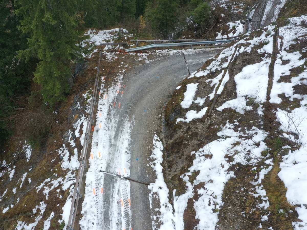 Die Alpstrasse mit Pneuabdruckspuren der Arbeitsmaschine im Schnee. Im Hintergrund der durchbrochene Bündnerzaun.