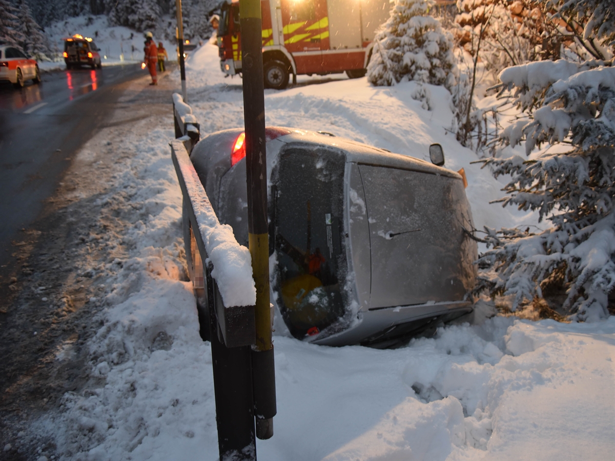 Im Vordergrund in der Bildmitte das Auto neben der Strasse im Schnee. Im Hintergrund ein Einsatzfahrzeuge von Feuerwehr und Polizei.