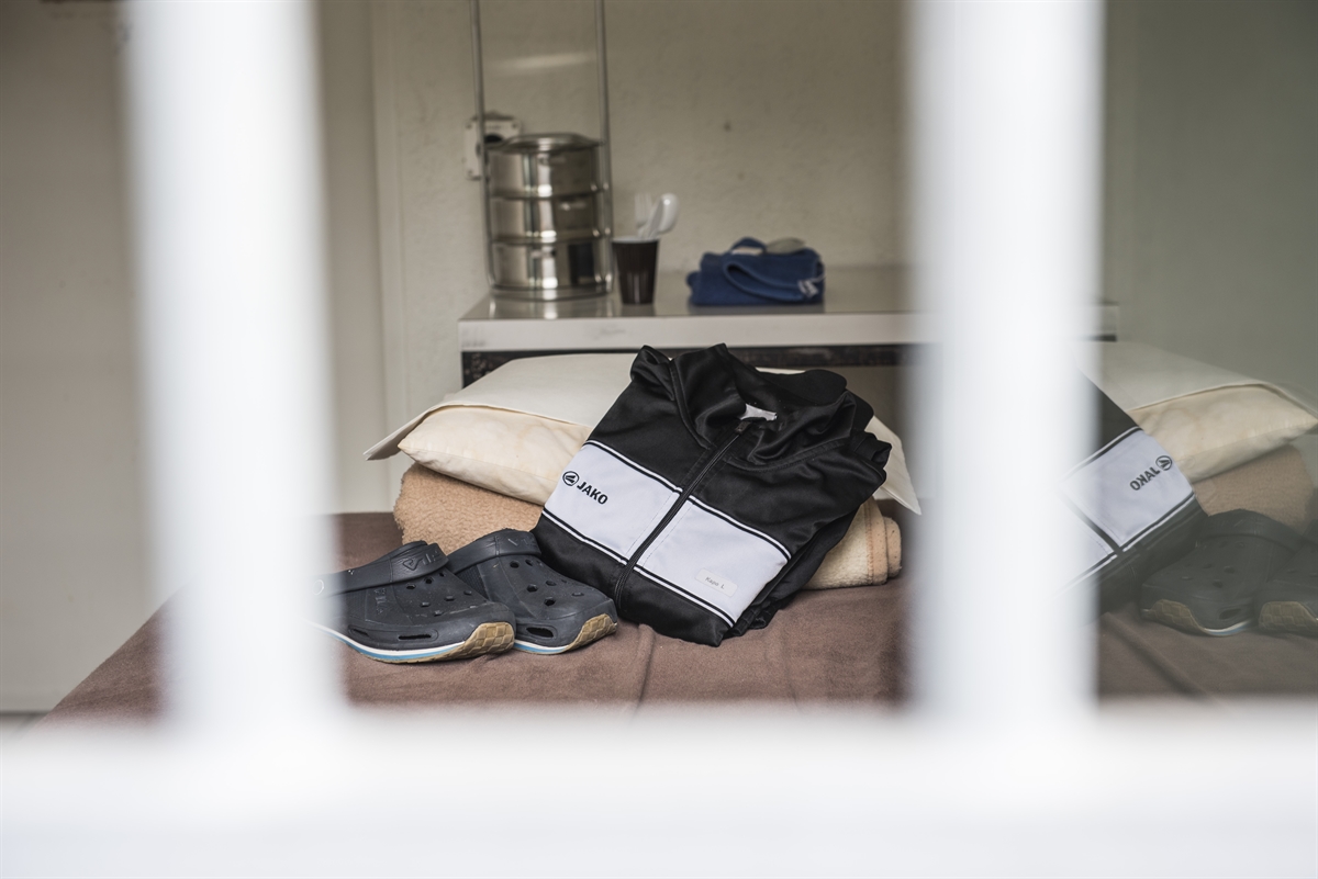 Blick zwischen Gitterstäben in die Zelle mit Trainer und Hausschuhen