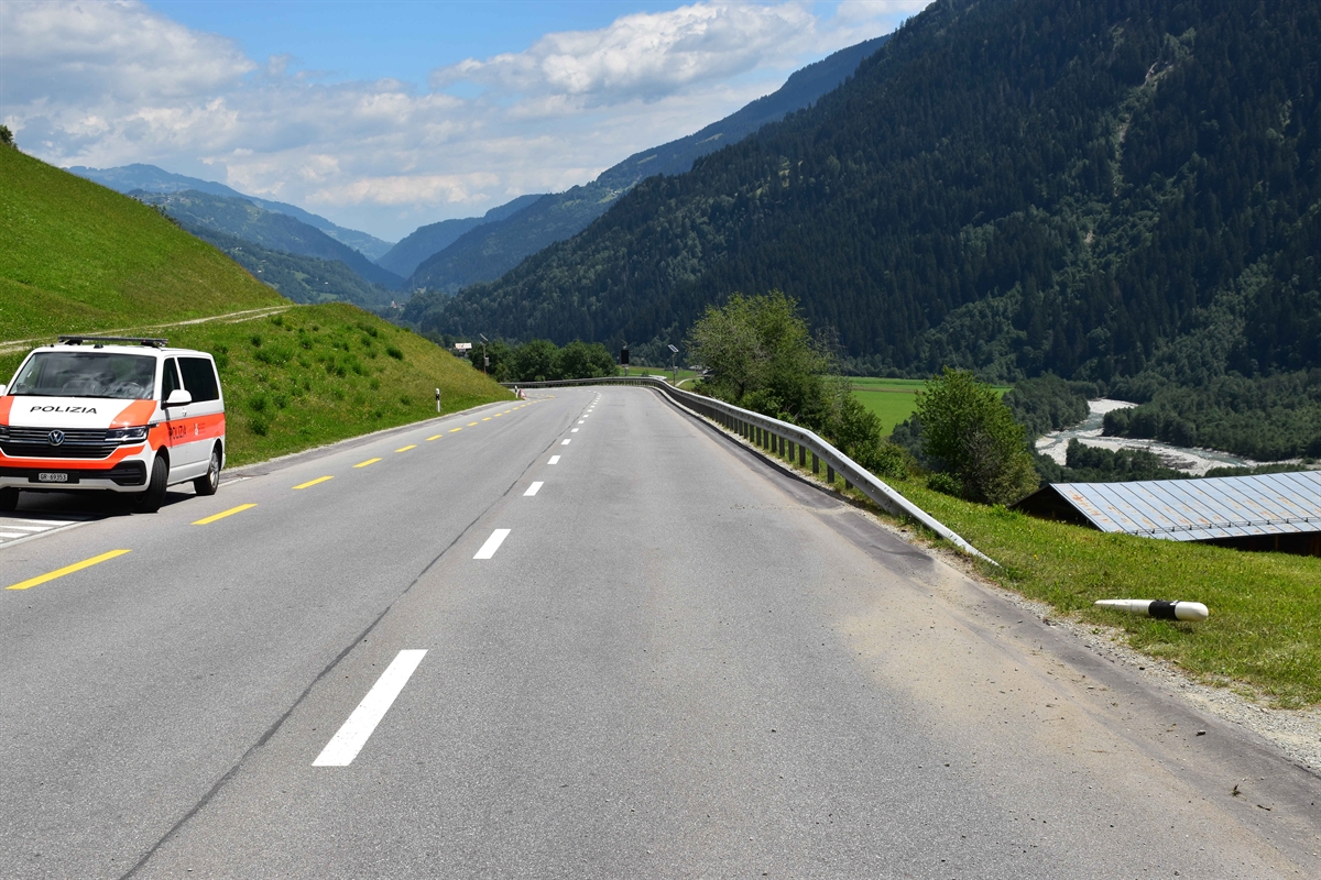Oberalpstrasse in Richtung Sumvitg. Am linken Strassenrand ein Patrouillenfahrzeug der Polizei abgestellt. Im Hintergrund leicht bewölkter Himmel und Berge zu erkennen. Auf der rechten Strassenseite ein beschädigter Leitpfosten bei der Kollisionsstelle mit der Leitplanke.