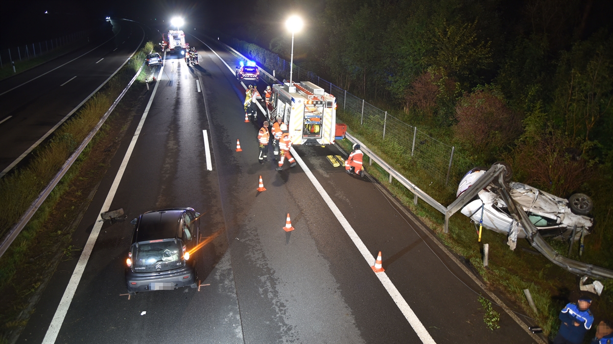 Strassenverlauf der Autobahn A13 im Bereich der Unfallstelle in Fahrtrichtung Chur gesehen. Vorne links das erste beteiligte Fahrzeug auf der Überholspur zu erkennen. Auf der rechten Seite zwischen der Leitplanke und dem Wildzaun das auf der Seite liegende zweite beteiligte Fahrzeug. Im Hintergrund noch drei Einsatzfahrzeuge der Polizei und Feuerwehr und das dritte beteiligte Fahrzeug