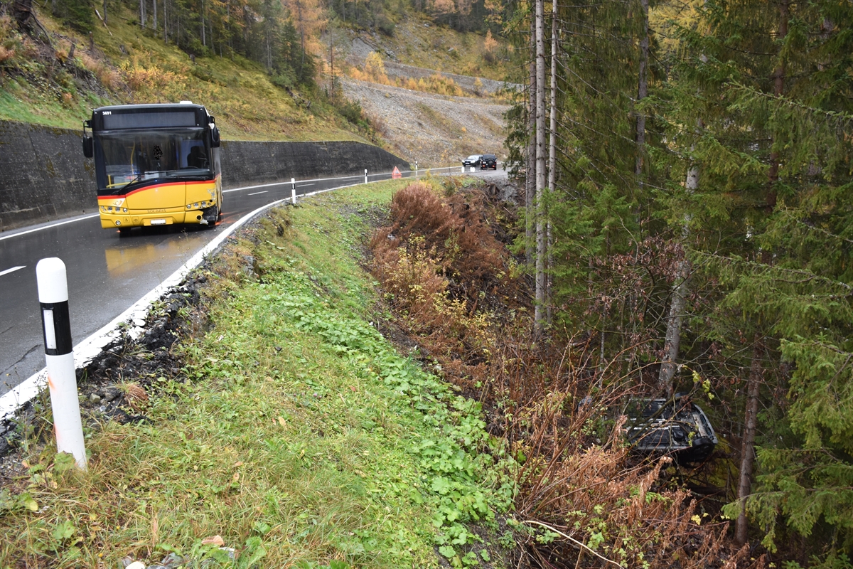 Postauto steht inmitten der Fahrbahnen und unterhalb der Strasse liegt ein Personenwagen auf dem Dach